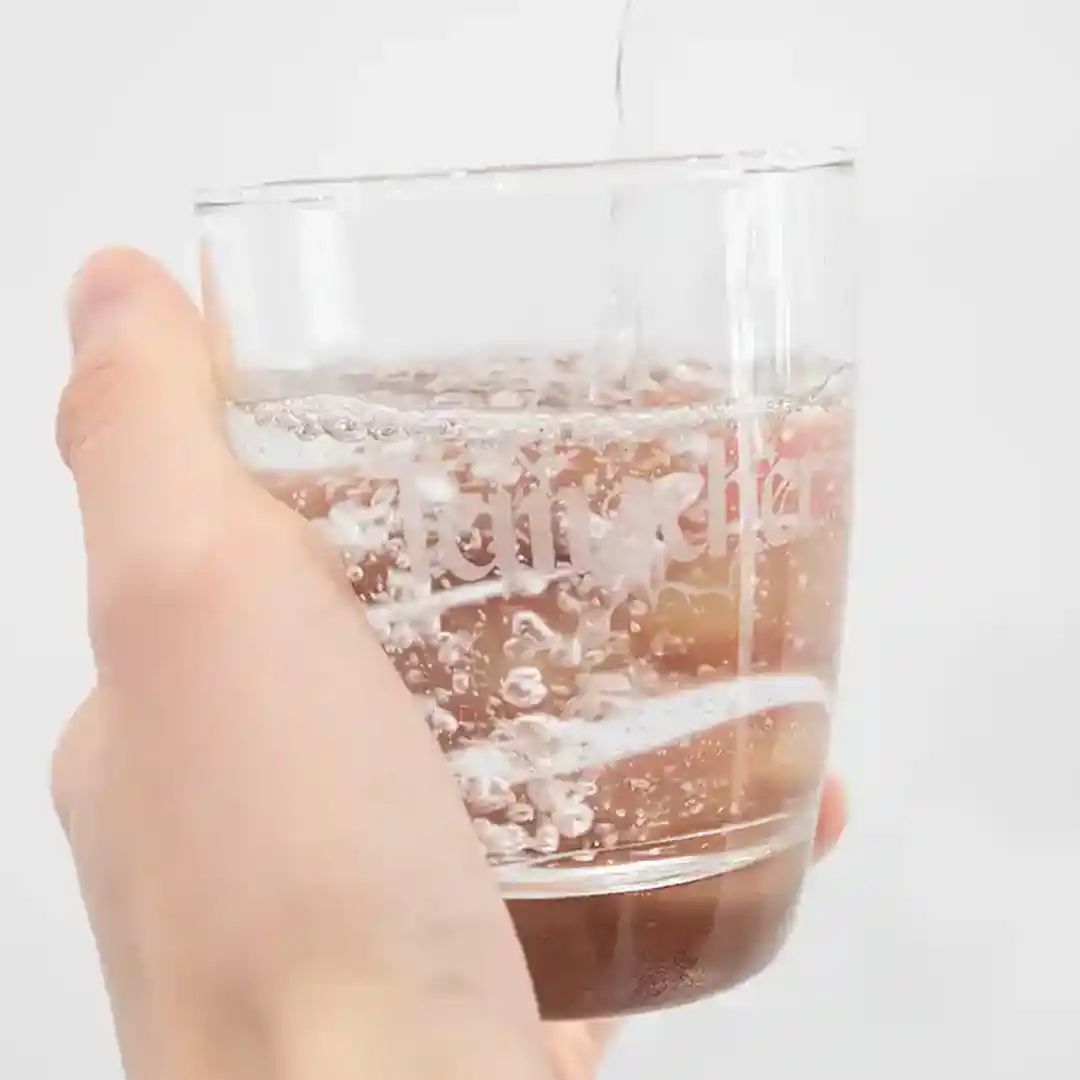 Hand hält ein Glas, in das sprudelndes Teinacher Mineralwasser aus einer Flasche gegossen wird