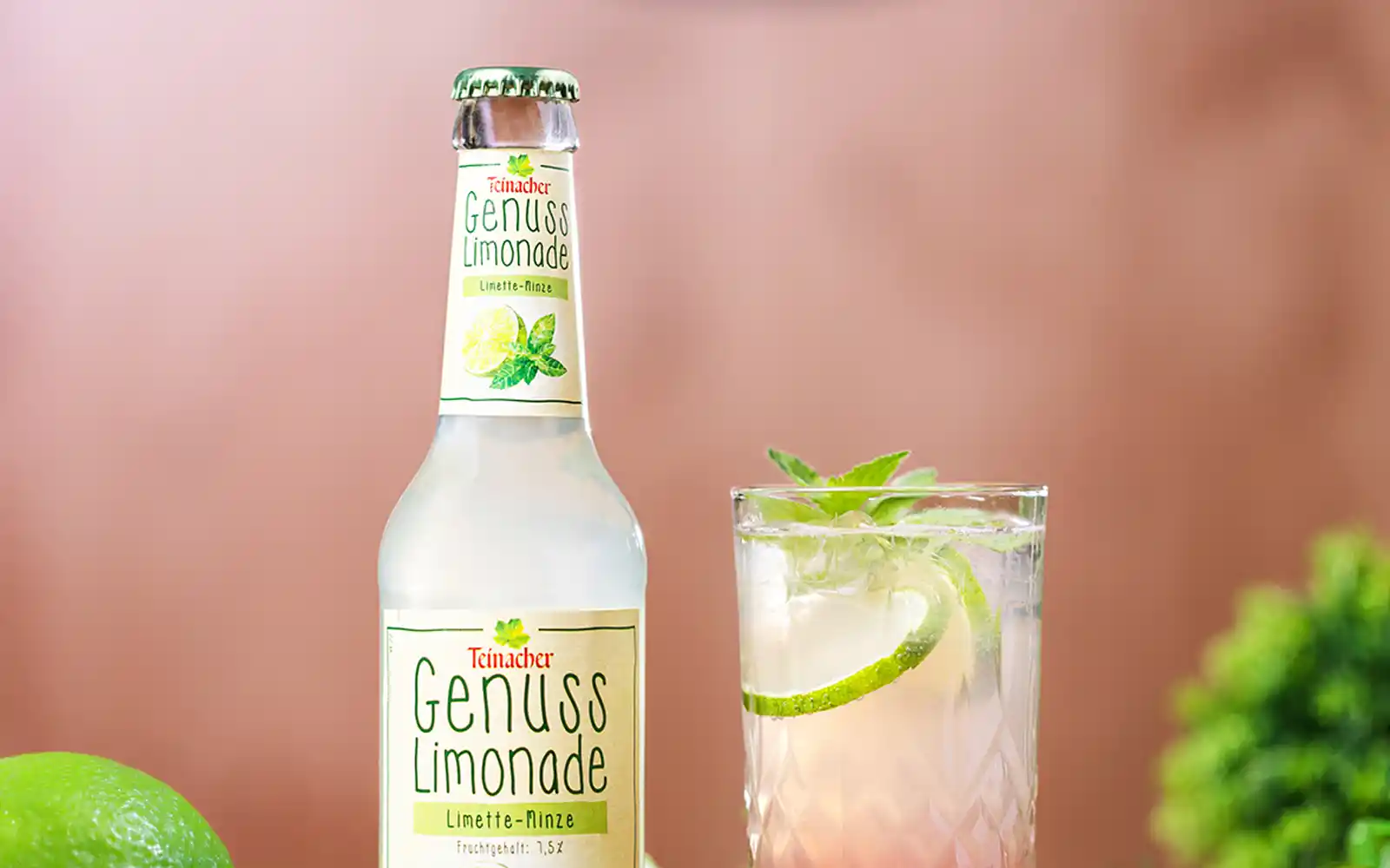 Teinacher Genusslimonade Limette-Minze neben einem Glas Mocktail mit Limettenscheiben und Minze auf grünem Untergrund in der Nahansicht