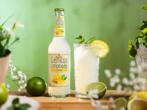 Nahaufnahme der Teinacher Genusslimonade Limette-Minze mit Glas Summer Spritz, Limettenscheiben und Strohhalm.