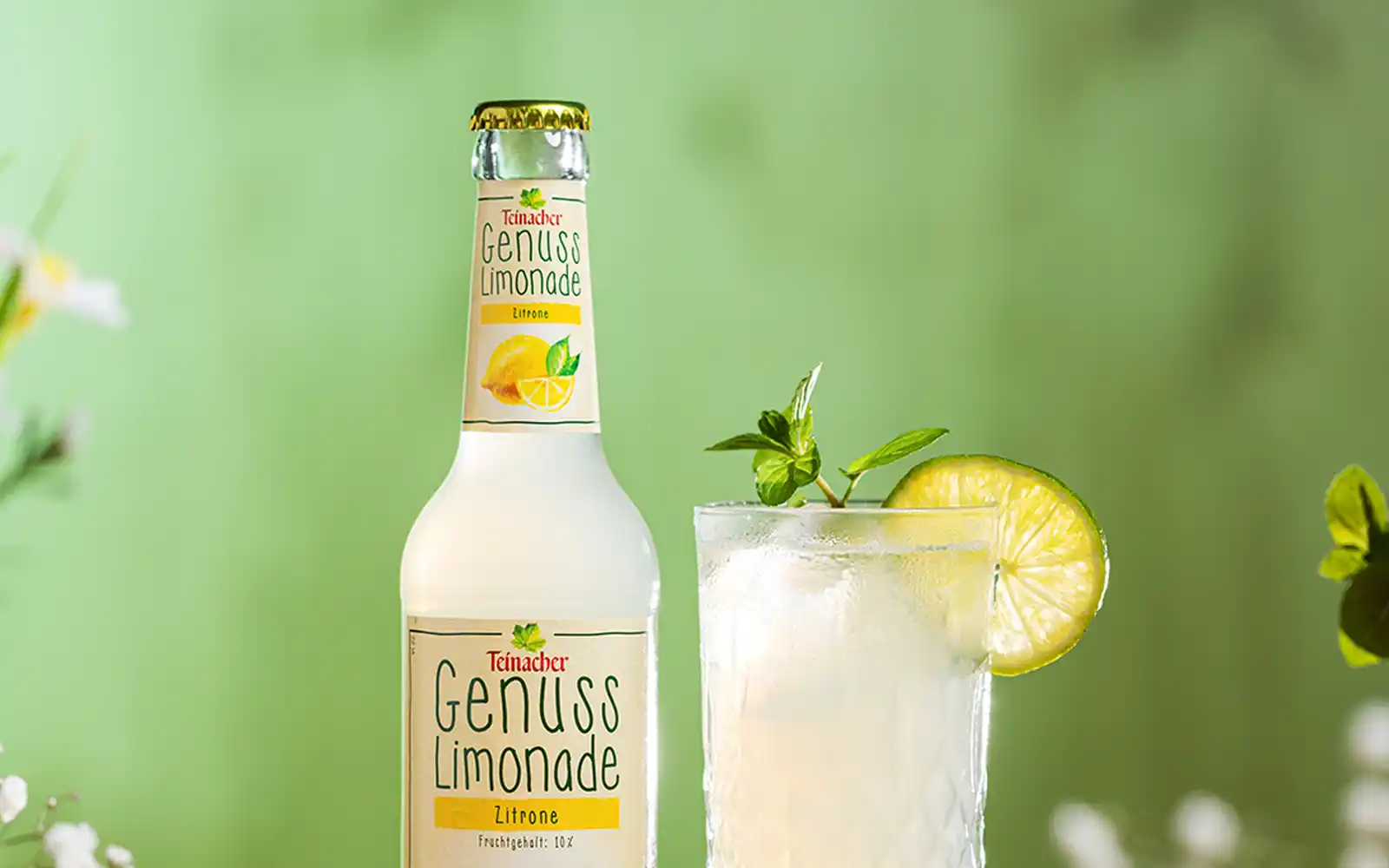 Nahaufnahme der Teinacher Genusslimonade Limette-Minze mit Glas Summer Spritz, Limettenscheiben und Strohhalm.