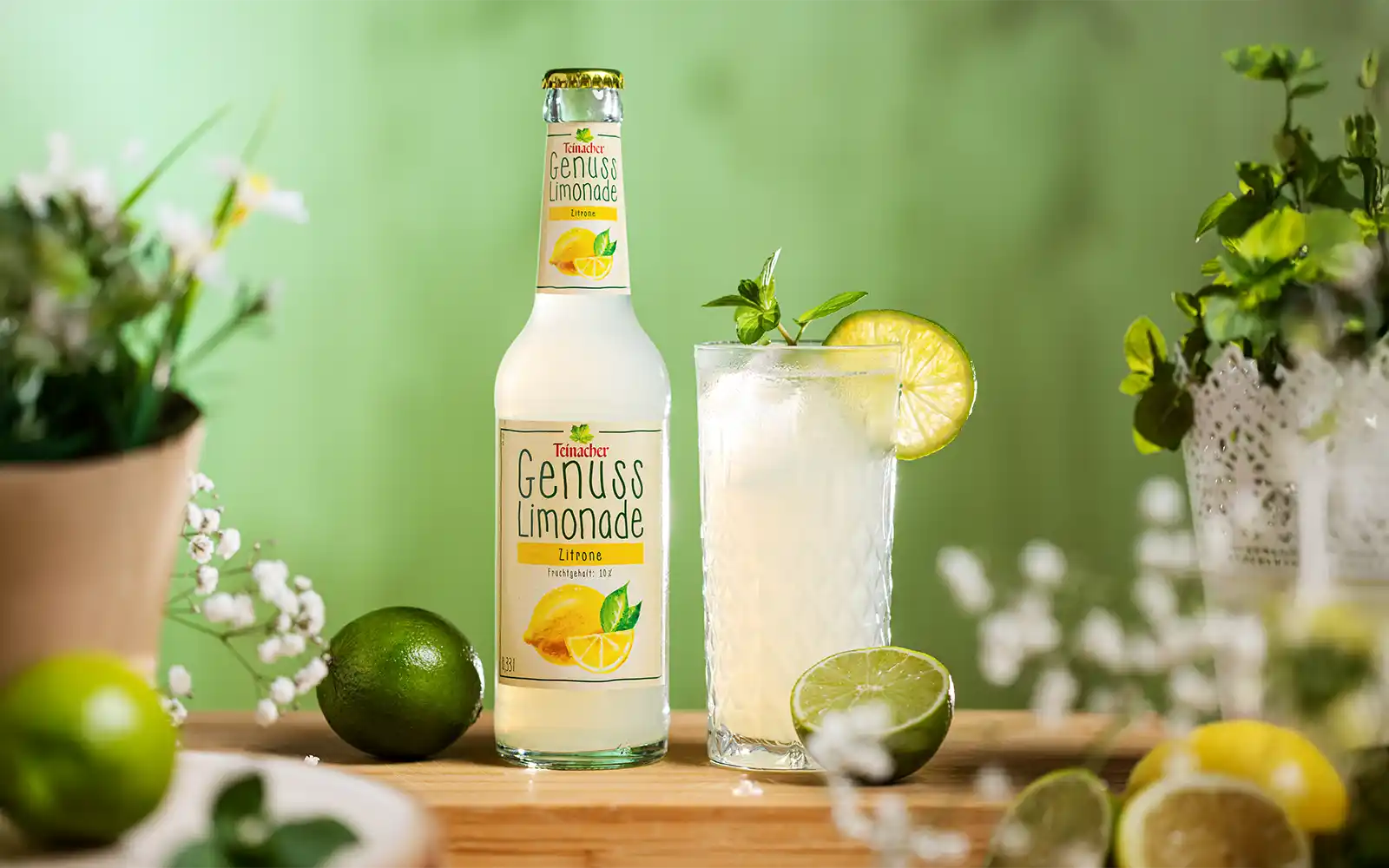 Nahaufnahme der Teinacher Genusslimonade Limette-Minze mit Glas Summer Spritz, Limettenscheiben und Strohhalm.