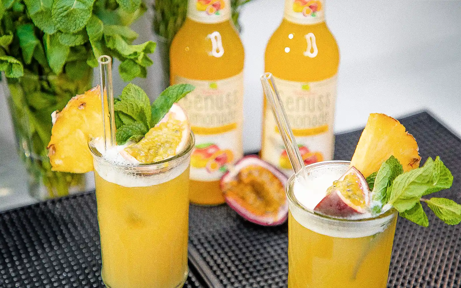 Teinacher Longneck Flaschen Genuss-Limonade Mango-Maracuja-Orange mit 2 Gläsern gefüllt mit Eiswürfeln und Früchten