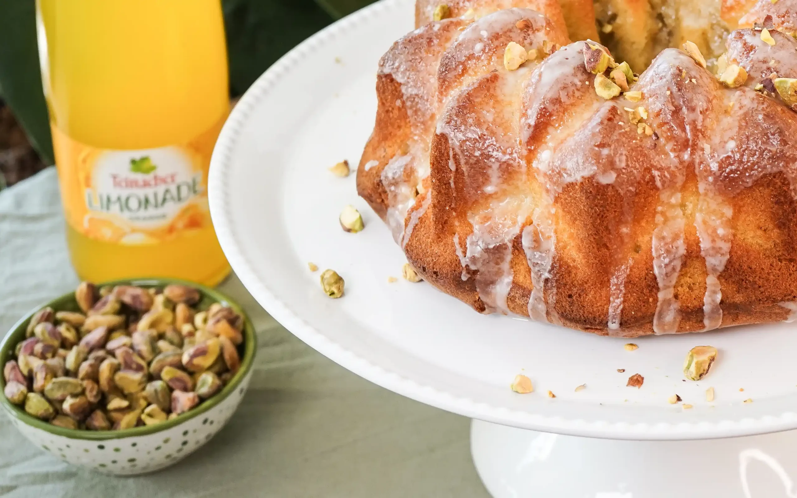 Teinacher Longneck Flaschen Genuss-Limonade Mango-Maracuja-Orange mit 2 Gläsern gefüllt mit Eiswürfeln und Früchten in der Nahaufnahme 